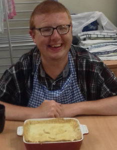 A person with learning disabilities smiling at a table with a pie they cooked