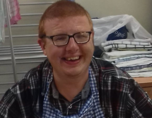 A person with learning disabilities smiling at a table with a pie they cooked