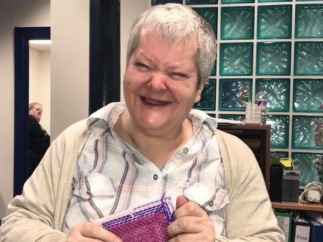 A person with learning disabilities smiling and holding a piece of decorated fabric