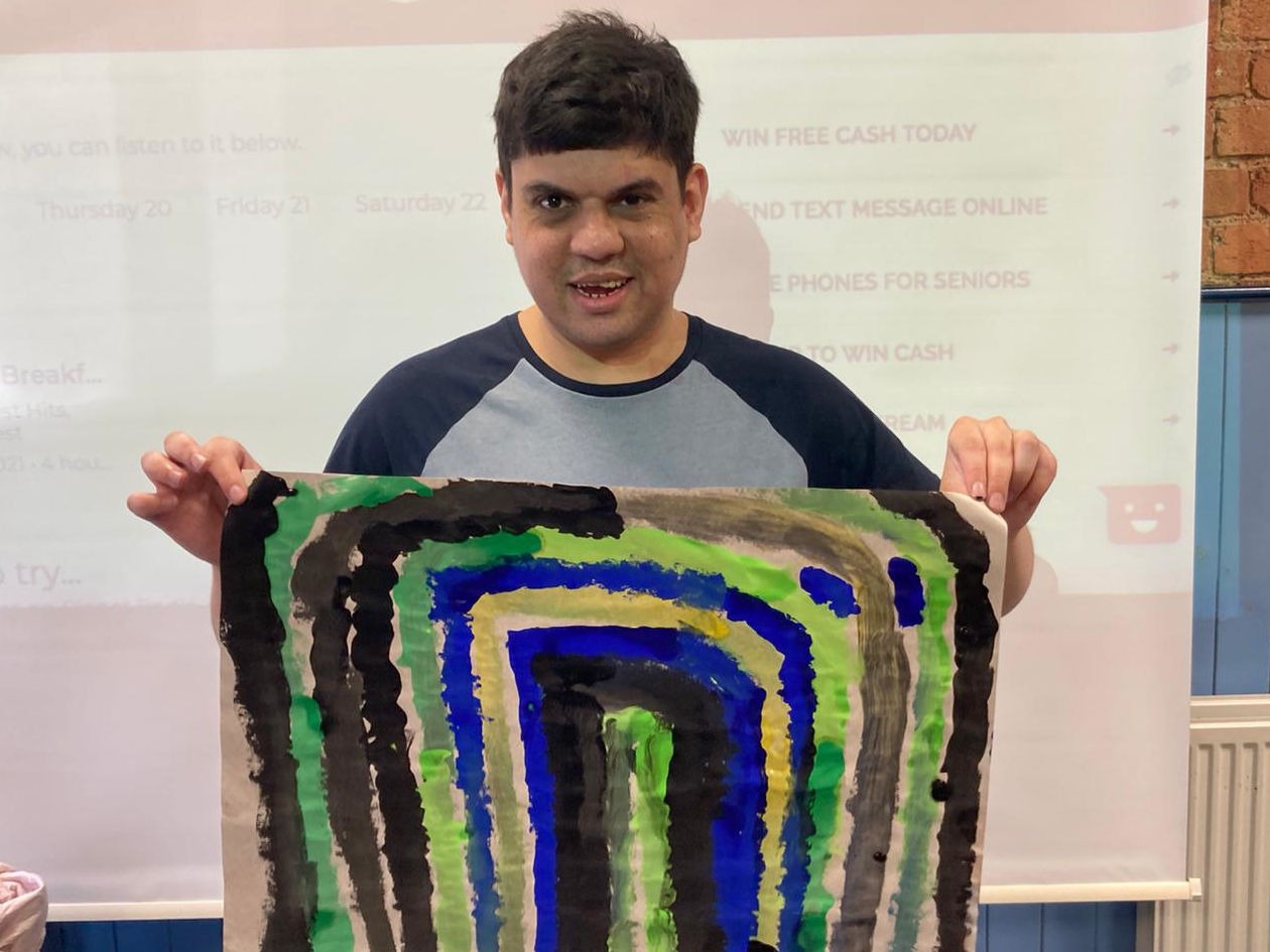 A person with learning disabilities holds a picture of a rainbow that he painted